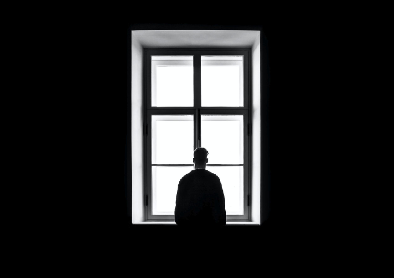 Black and white image of the back of a man staring out a window